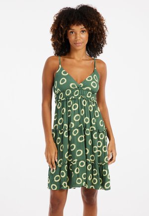 Vestido de verano verde con un diseño en capas, que presenta grandes patrones circulares de color claro, tirantes finos y una textura acanalada.