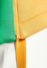 Gros plan d'une fermeture éclair jaune partiellement ouverte sur un tissu vert et jaune avec une sangle jaune texturée en dessous.