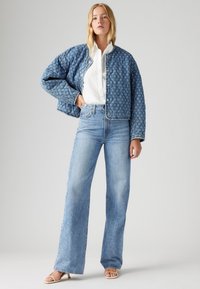 Veste en denim matelassée dans une teinte bleue, avec un col rond, des boutons-pression et une coupe courte, associée à des jeans évasés bleu clair.