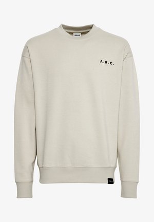 Beige puuvillane sviiter, millel on ümar kaelus, must "A.R.C." tekst vasakul rinnal, soonikkoes varrukate otstes ja allääres ning väike must silt külgmistel õmblustel.