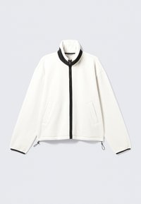 Chaqueta de forro polar blanca con cremallera negra en la parte delantera, cuello alto, dos bolsillos laterales y puños elásticos con toggles ajustables en el dobladillo.