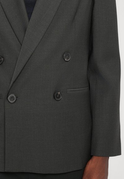 Διπλής όψης σκούρα γκρι σακάκι με υφή, διαθέτοντας τέσσερα μαύρα κουμπιά και μία πλαϊνή τσέπη.