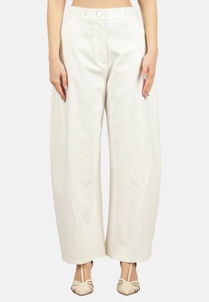 Donna che indossa pantaloni bianchi a vita alta e gamba larga con chiusura frontale con bottoni e zip, abbinati a tacchi beige con punta appuntita.