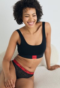 Soutene nero e slip in pizzo nero con vita rossa "HUGO". Il tessuto è liscio con un motivo testurizzato sugli slip.
