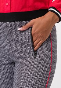 Leggings à motif noir et blanc avec une poche zippée, une ligne d'accent rouge et une taille élastique texturée. Gros plan sur les détails du tissu.