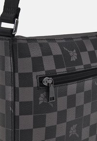 Borsa a scacchi nera e grigia realizzata in pelle texturizzata, con una tasca frontale con zip e decorazioni floreali.