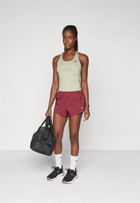 Ljusgrön sporttopp, vinröda shorts, svarta sneakers, vita strumpor. Håller i en svart gymväska. Har Puma-logotypen på kläderna och väskan.