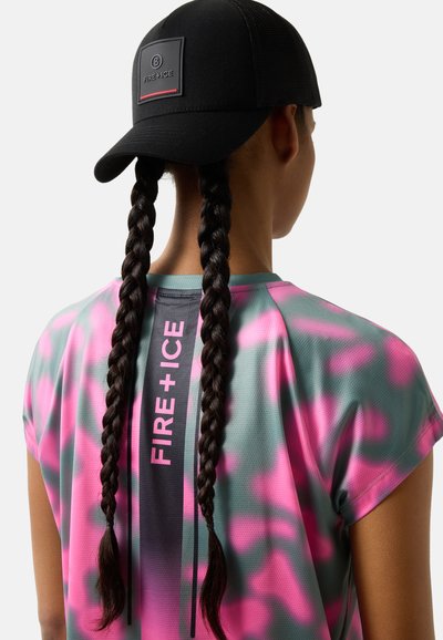 Personne avec deux longues tresses porte une casquette noire et une chemise à motifs rose et gris avec le texte vertical « FIRE+ICE » dans le dos.