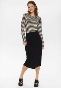 Schwarze Midi-Rock mit einem eleganten, taillierten Design, kombiniert mit einem langärmeligen Oberteil mit horizontalen Streifen in Beige und Dunkelbraun. Schwarze Plateauschuhen.