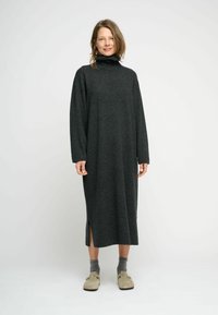 Rochie din tricot cu mânecă lungă, de culoare gri închis, confecționată dintr-un material moale. Prezintă slițuri laterale și este asortată cu șosete gri și încălțăminte ușoară de culoare deschisă.