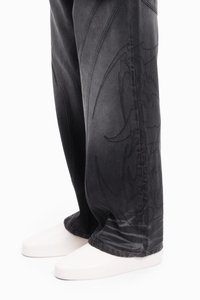 Pantaloni din denim negri cu modele tonale complexe, o croială lejeră și pantofi albi cu suprafață netedă.