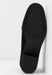 Semelle de chaussure plate noire avec une texture lisse et un léger talon, présentée sur fond blanc.