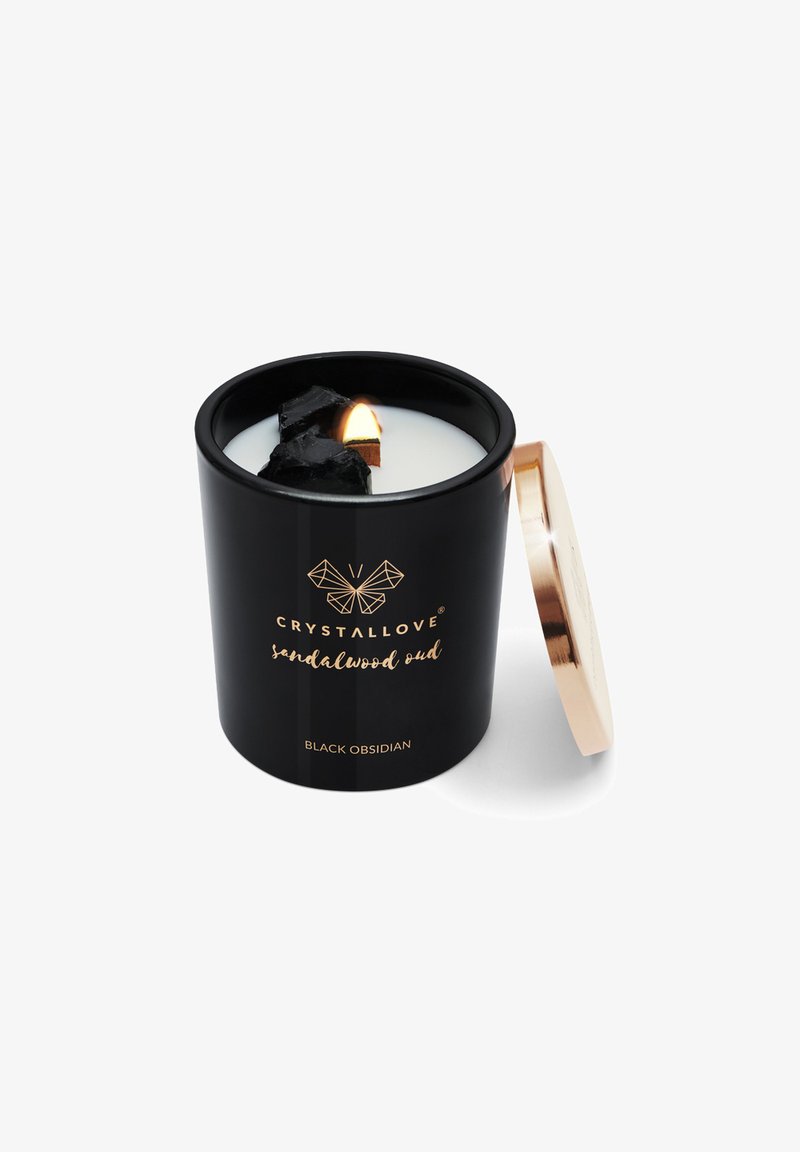 Czarna świeca z złotą pokrywką, z białym woskiem w środku i kawałkami czarnego obsydianu. Etykieta głosi "CRYSTALLOVE sandałowe oud."