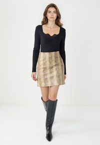 Zwarte long sleeve top met kantaccenten, gecombineerd met een gouden slangenprint minirok en knielange zwarte leren laarzen. Gladde texturen overal.