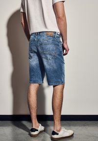 Jeansshorts i ljusblått med en urtvättad finish, med bakfickor och bälteshällor. Matchat med vita sneakers, mot en neutral bakgrund.