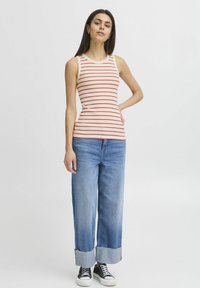 Top sans manches rayé en crème et rouge, associé à un jean bleu à jambes larges, avec des ourlets effilochés et des baskets noires.