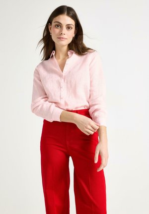 Helles rosa Leinenhemd mit langen Ärmeln und Knopfleiste, kombiniert mit lässigen, hochgeschnittenen roten weitem Hosen. Glatte Textur, schlichtes Design.