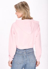 Gekürzter rosa Hoodie mit glatter Textur, langen Ärmeln und verstellbarer Kapuze, kombiniert mit hochgeschnittenen blauen Jeans.