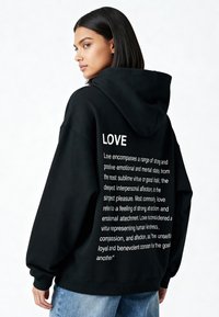 Svart hoodie med stor "LOVE"-text tryckt på baksidan, med en mjuk textur, avslappnad passform och ribbade mudd.
