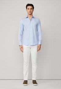 Camisa de botones a rayas azul claro con mangas largas, combinada con pantalones blancos y zapatos marrones. Tejido suave con un diseño de cuello clásico.