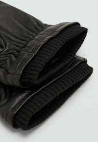 Guanti in pelle nera con polsini in maglia nera a coste. Texture liscia con dettagli di cuciture sottili e vestibilità aderente al polso.