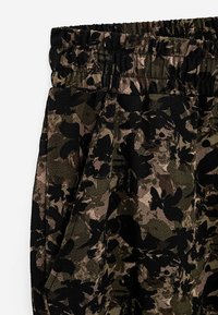 Donkergroene en bruine camouflagepatroon broeken met een elastische tailleband en zijzakken. De stof heeft een gestructureerde afwerking.