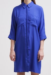 Blue, short-sleeve dress made of smooth fabric with a button-down front, featuring two chest pockets and a collar.