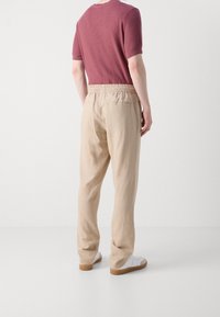 Beige linnebyxor med elastisk midja och bakfickor, kombinerat med en vinröd kortärmad skjorta och vita sneakers.