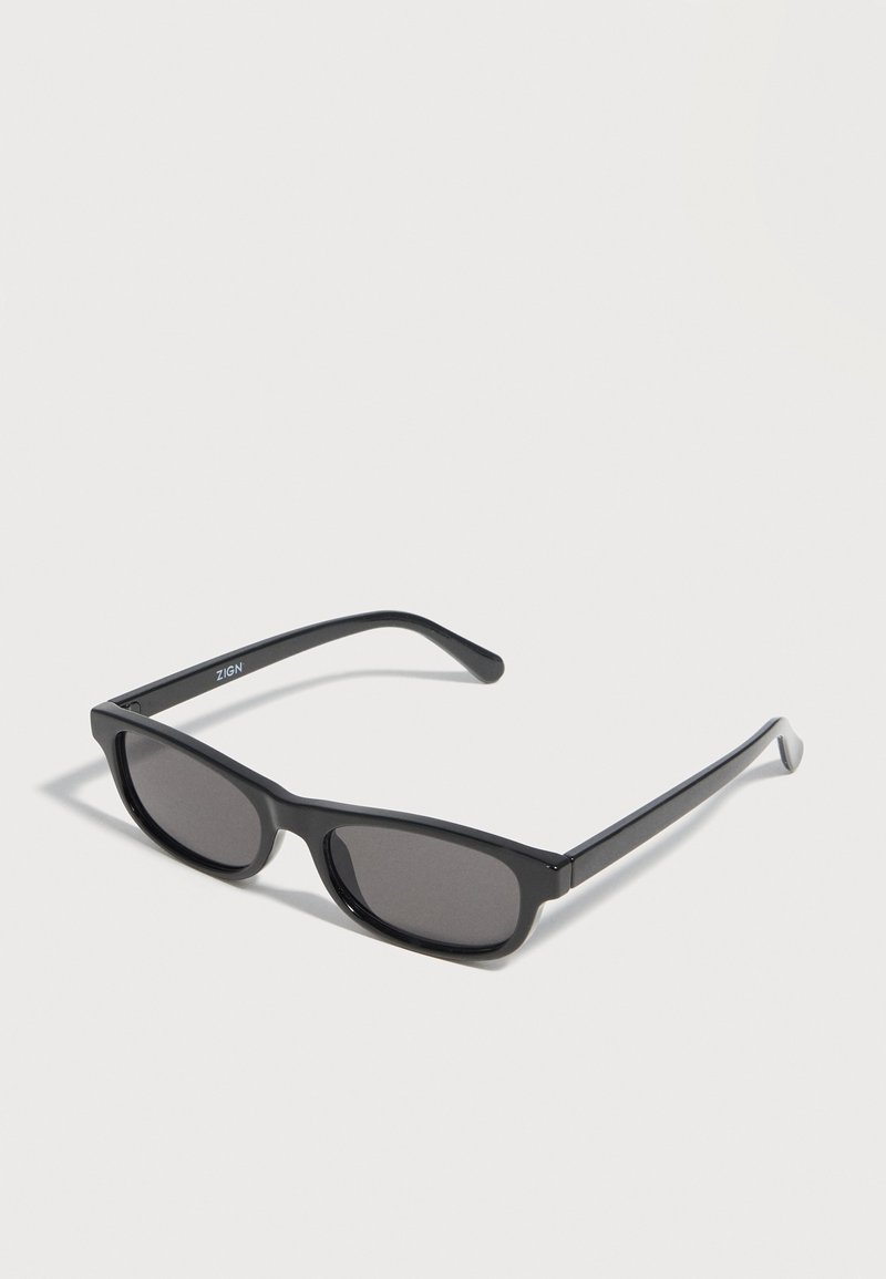 Μαύρα ορθογώνια γυαλιά ηλίου με σκούρους φακούς και λεπτούς βραχίονες, παρουσιασμένα σε απλό ανοιχτό φόντο.