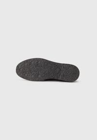 Sole of a black shoe with round grip patterns and textured rubber surface, shown from bottom view on a white background.