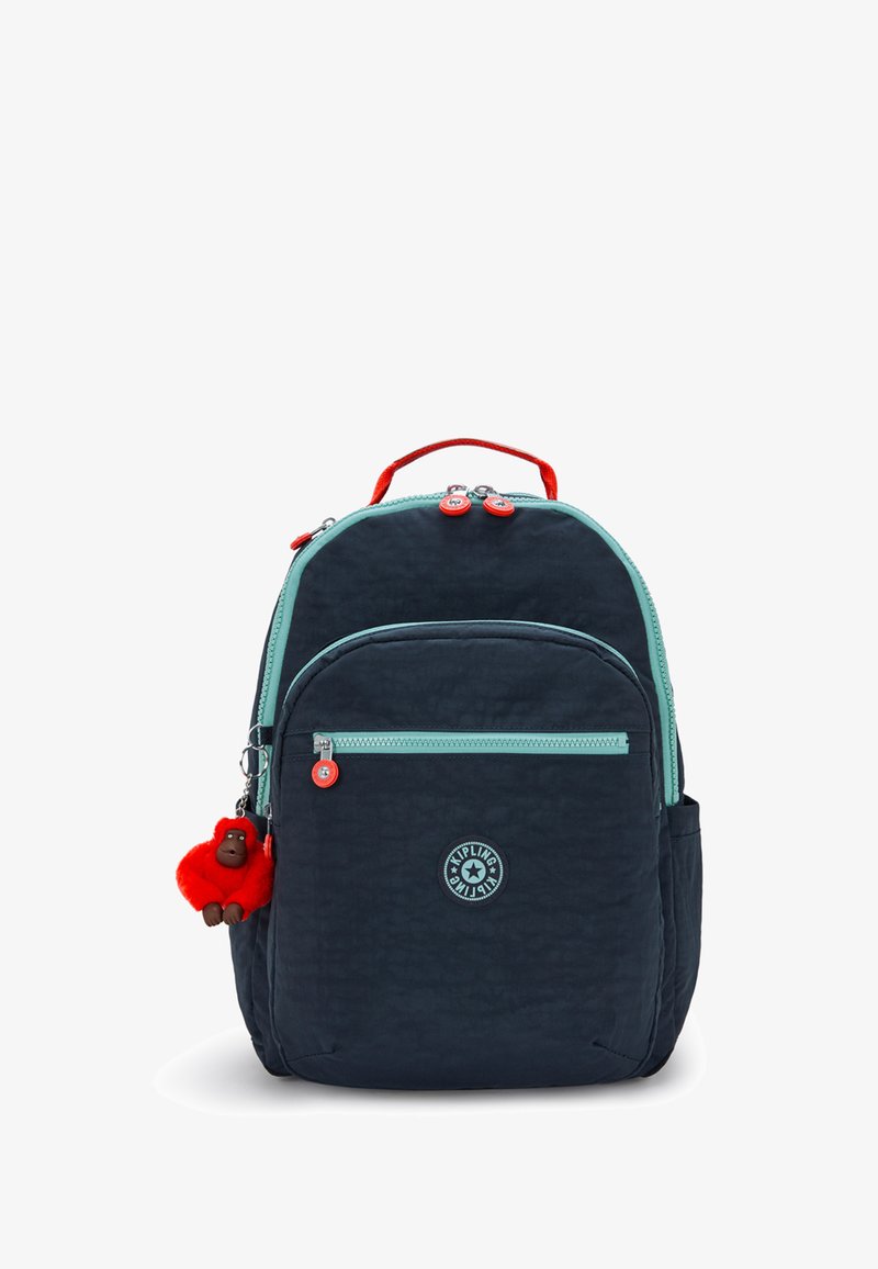 Tmavěmodrý batoh s texturovaným povrchem, mátově zeleným zipem, červenými akcenty a podivným klíčenkou ve tvaru opice. Obsahuje několik kapsiček a pevnou rukojeť.