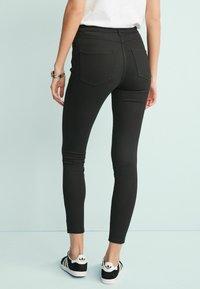 Svarta tajta jeans med hög midja, med en slank design och standard bakfickor. Bärs med svarta och vita sneakers.