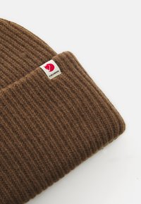 Brown ribbed knit beanie with folded cuff and small white label featuring a red fox head logo and black brand text.