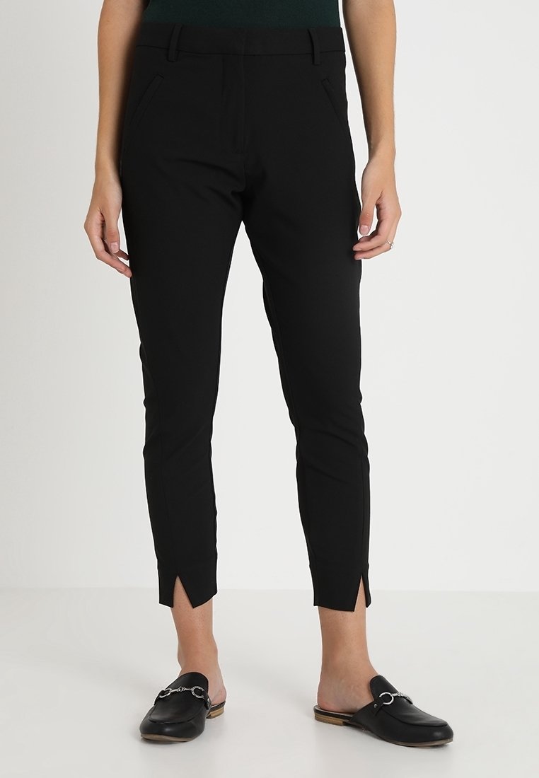 Svarta åtsittande byxor i stretchmaterial, med smala ben och sidosslitsar vid fållen samt två framfickor. Ett par svarta slip-on skor.