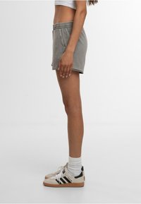 Shorts en coton gris avec une taille élastique, des poches latérales et une coupe décontractée, associés à des baskets crème et des chaussettes blanches.