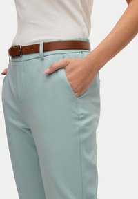 Pantaloni azzurri chiari realizzati in un tessuto testurizzato, dotati di tasche laterali e di una cintura in vita elastica, accompagnati da una cintura in pelle marrone.