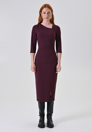 Bordeaux figuuraccentuerend jurkje met driekwartmouwen, asymmetrische halslijn en een zijsplit, gecombineerd met kniehoge zwarte laarzen.