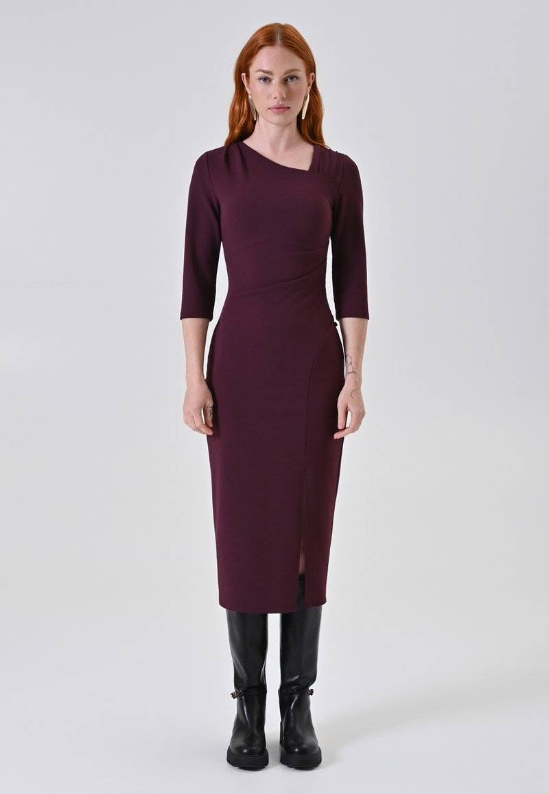 Bordeaux figuuraccentuerend jurkje met driekwartmouwen, asymmetrische halslijn en een zijsplit, gecombineerd met kniehoge zwarte laarzen.