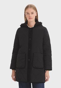 Manteau noir matelassé avec capuche, doté d'un doux bord en fausse fourrure, de boutons sur le devant et de deux grandes poches avant.