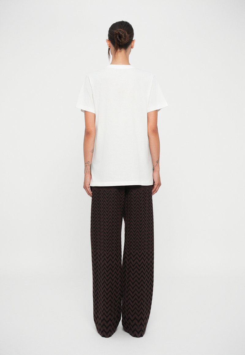 T-shirt bianco a maniche corte e pantaloni larghi marroni con motivo, caratterizzati da un design a chevron e tessuto testurizzato, visti da dietro.
