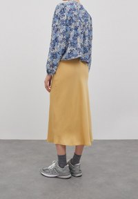 Top floreale con maniche a palloncino, gonna midi gialla, sneakers grigie e calze. Risulta casual con una vestibilità rilassata e texture morbide.
