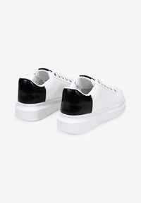 Sneaker bianche con finitura in pelle liscia e dettagli in pelle nera testurizzata sul tallone, dotate di un design con lacci e suola spessa bianca.