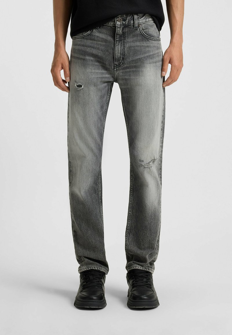 Faded black denim jeans with a straight leg, featuring distressed detailing and subtle whiskering. Paired with black sneakers.