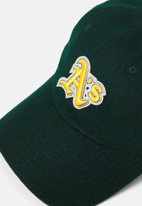 Grön ullbasebollkeps med en broderad gul "A's"-logotyp med vita accenter på framsidan. Slät textur och böjd skärm.