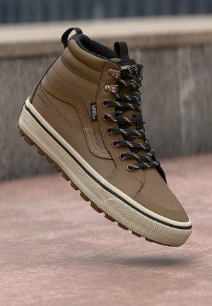 Brown waterproof high-top sneaker with a textured finish, black and white laces, and a rubber sole featuring a grippy pattern. Stylish stitching accents.