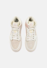 Paire de baskets montantes beige clair et blanches avec des boîtes à orteils perforées et des lacets blancs vues de dessus sur un fond blanc.