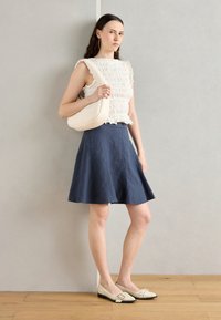 White smocked top, dark blue flared skirt, and beige flat shoes with black tip. Complemented by a small cream shoulder bag.