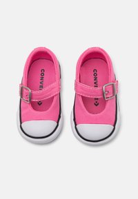 Zapatillas de lona rosa con puntera redondeada, suela de goma blanca, correa ajustable con hebilla y detalles en negro a lo largo de los laterales.