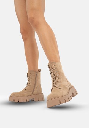 Bottines beiges en daim, avec une semelle épaisse, un laçage à l'avant et une fermeture éclair sur le côté pour un enfilage facile.
