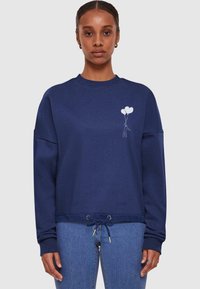 Felpa blu navy con collo a giro, spalle abbassate e orlo con cordino elastico. Presenta una grafica di un palloncino bianco sul petto.